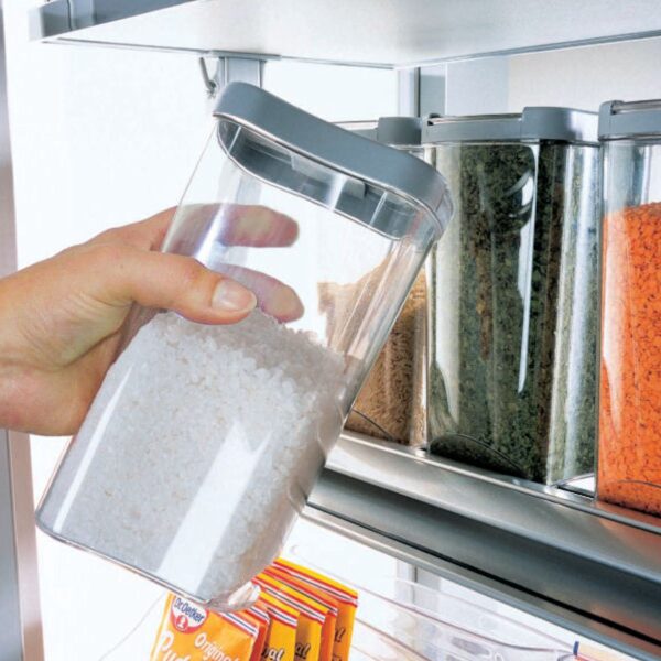 Eine Hand entnimmt eine klare Vorratsdose aus einem Regal mit ähnlichen Behältern - Teil des Vorratsdosen-Sets für DISPENSA-X, DISPENSA Swing-ideal für platzsparende Aufbewahrung von getrockneten Lebensmitteln oder Gewürzen.