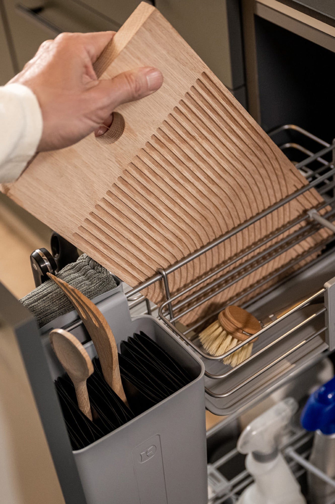 Hand nimmt ein Schneidebrett  aus einem Küchenunterschrank.