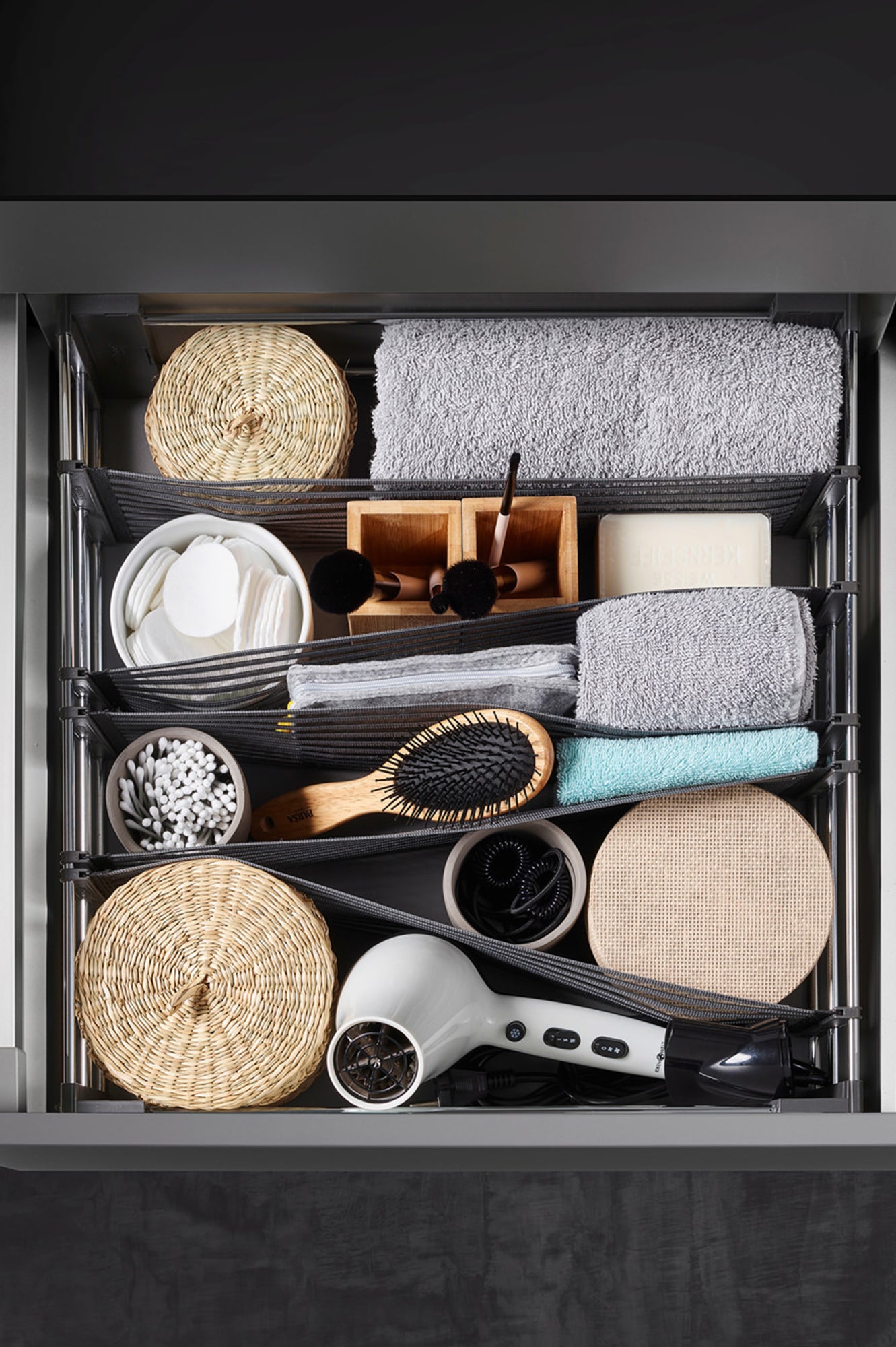 Offene Schublade von oben mit Schubladenorganizer, in dem Badezimmerutensilien und ein Föhn verstaut sind.