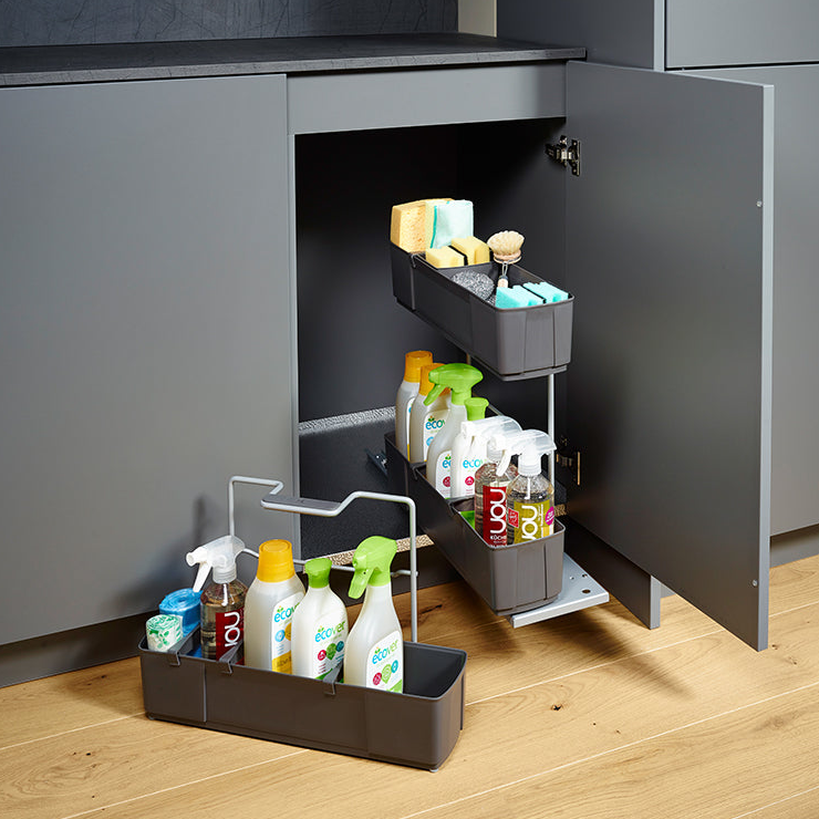 Ein grauer Küchenschrank ist offen und zeigt zwei Auszugsböden für Putzmittel. Davor sorgt der cleaningAGENT - Putzschrank Organizer & Putzmittelauszug für Ordnung auf dem Holzboden.