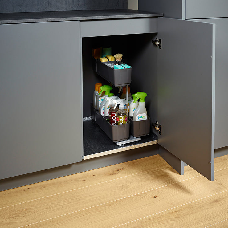 Ein offener grauer Schrank mit dem cleaningAGENT - Putzschrank Organizer & Putzmittelauszug zeigt unten Sprays und Flaschen und oben Pinsel und Schwämme, alles übersichtlich angeordnet. Der Schrank steht auf einem hellen Holzboden.