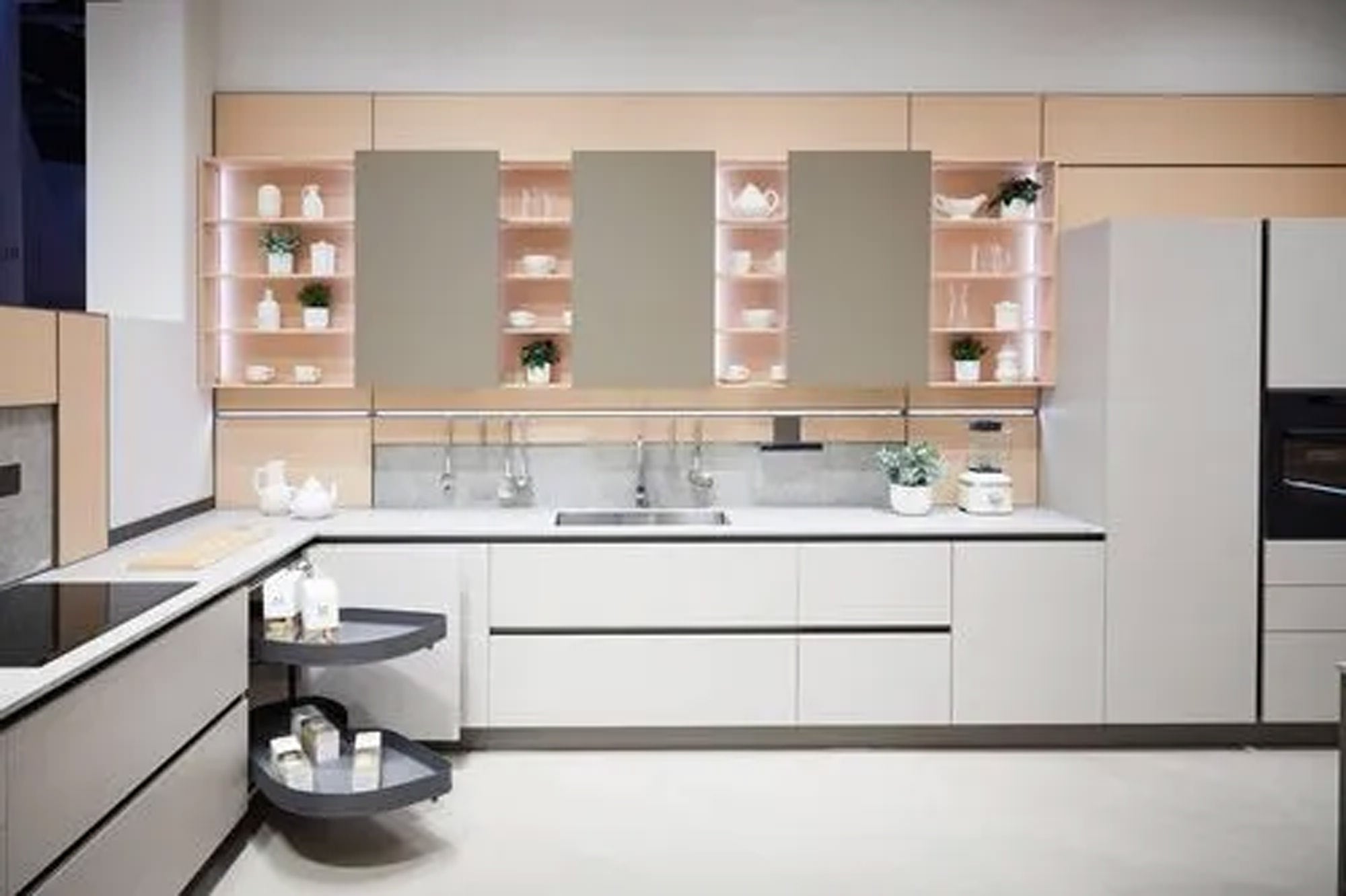 Moderne Küche mit hellen Schränken, glatten Arbeitsflächen, Einbaugeräten und offenen Regalen, in denen Geschirr und Topfpflanzen stehen. Ausziehbare Eckregale sind ausgezogen und bieten organisierten Stauraum.