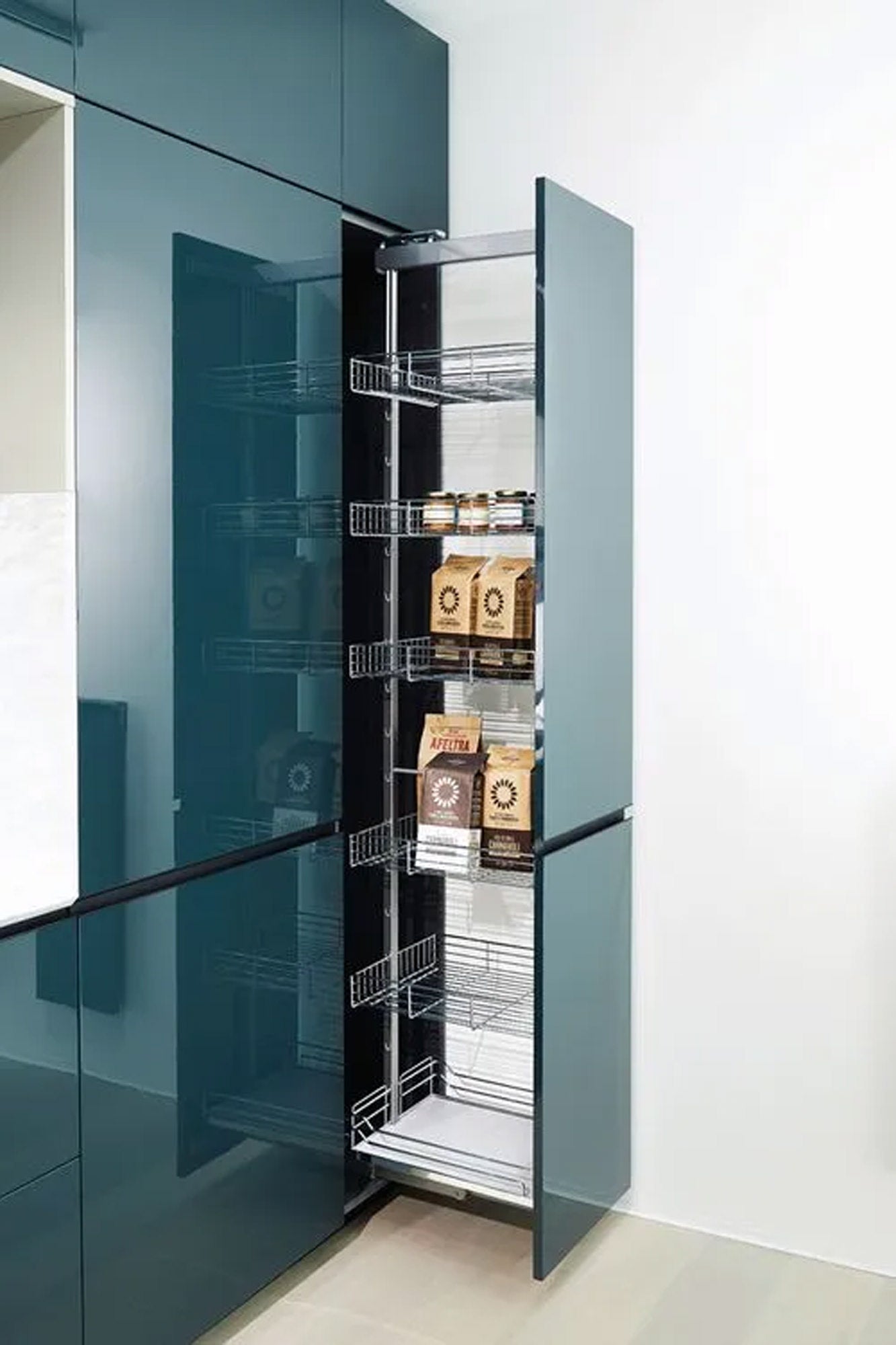 Ein hoher, glänzender blauer Küchenschrank ist geöffnet und gibt den Blick auf eine ausziehbare Speisekammer mit Metallregalen frei, in denen sich verschiedene braune Papierverpackungen für Lebensmittel befinden. Die Speisekammer ist ordentlich geordnet, die meisten Fächer sind leer.