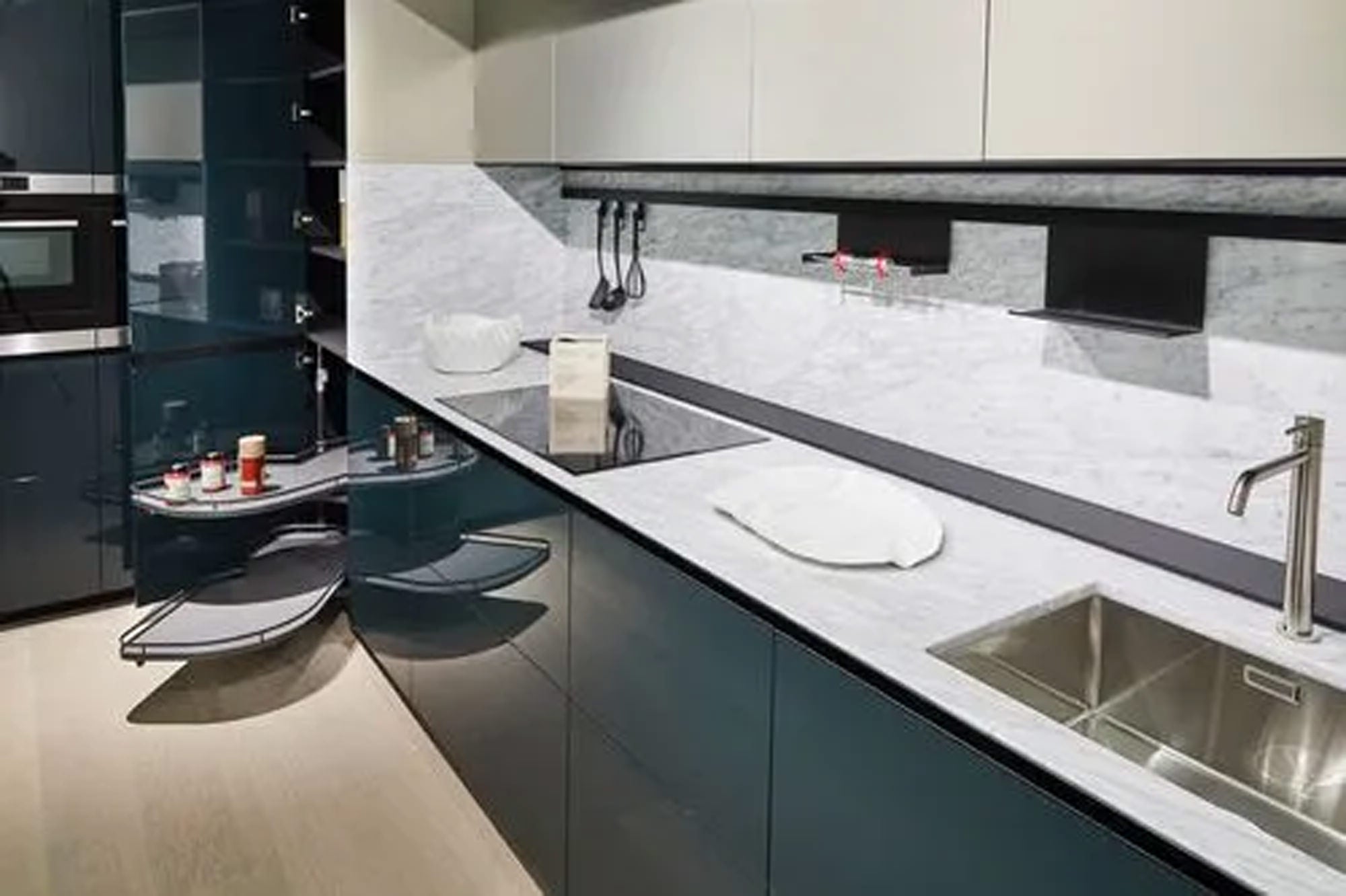 Moderne Küche mit glänzenden dunklen Schränken, Arbeitsplatte und Aufkantung aus Marmor, Edelstahlspüle, Induktionskochfeld und einem Eckschrank mit ausziehbaren Regalen für Gewürze und Gläser.