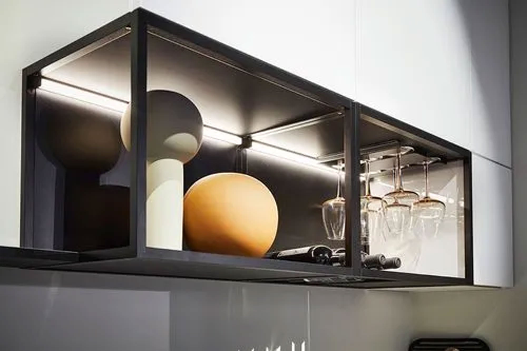 Ein modernes Küchenregal mit Glaswänden zeigt eine orangefarbene Kugelvase, eine weiße Skulptur, Weinflaschen und hängende Weingläser unter sanfter Deckenbeleuchtung.