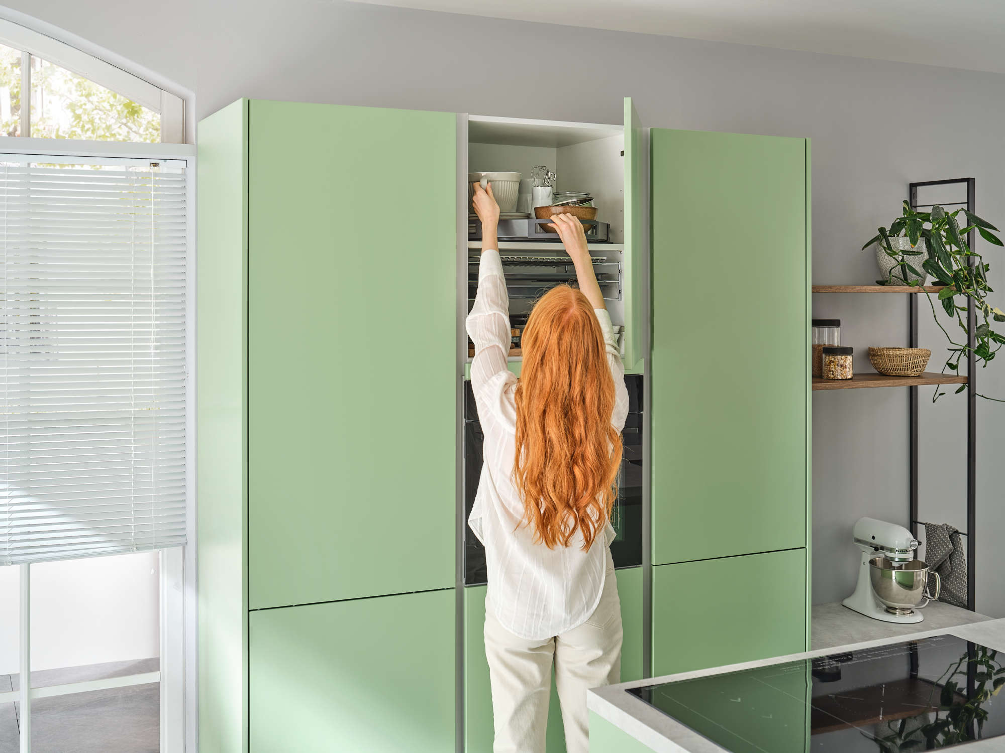 Frau holt aus geöffnetem Hochrank mit einem auf dem Zwischenbode montierten Drehtablar eine Schüssel.