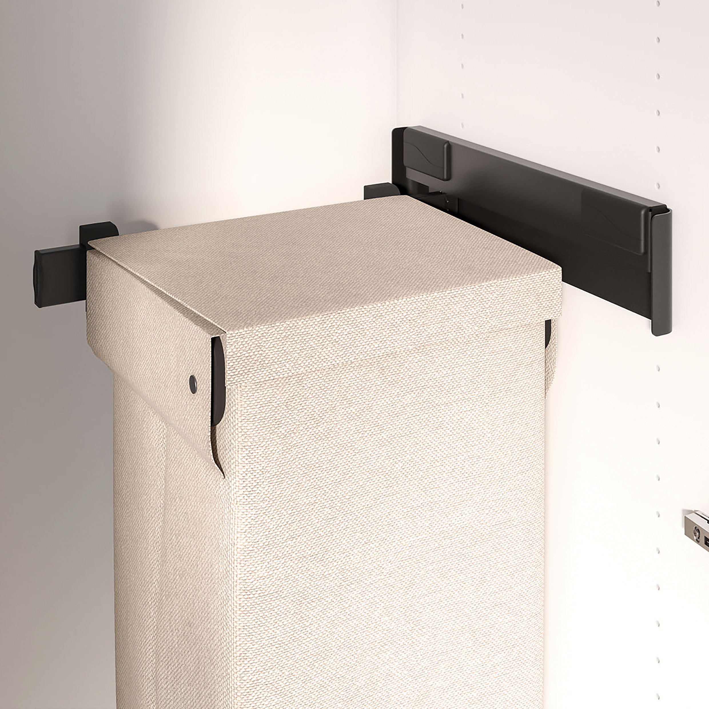 Ein beiger Stoffwäschesack mit Deckel wird mit dem CONERO Funktionsauszug für Wäschekorb, einem schwarzen Metall-Funktionsauszug, der an den Schrankwänden befestigt wird, in einen weißen Kleiderschrank eingebaut.