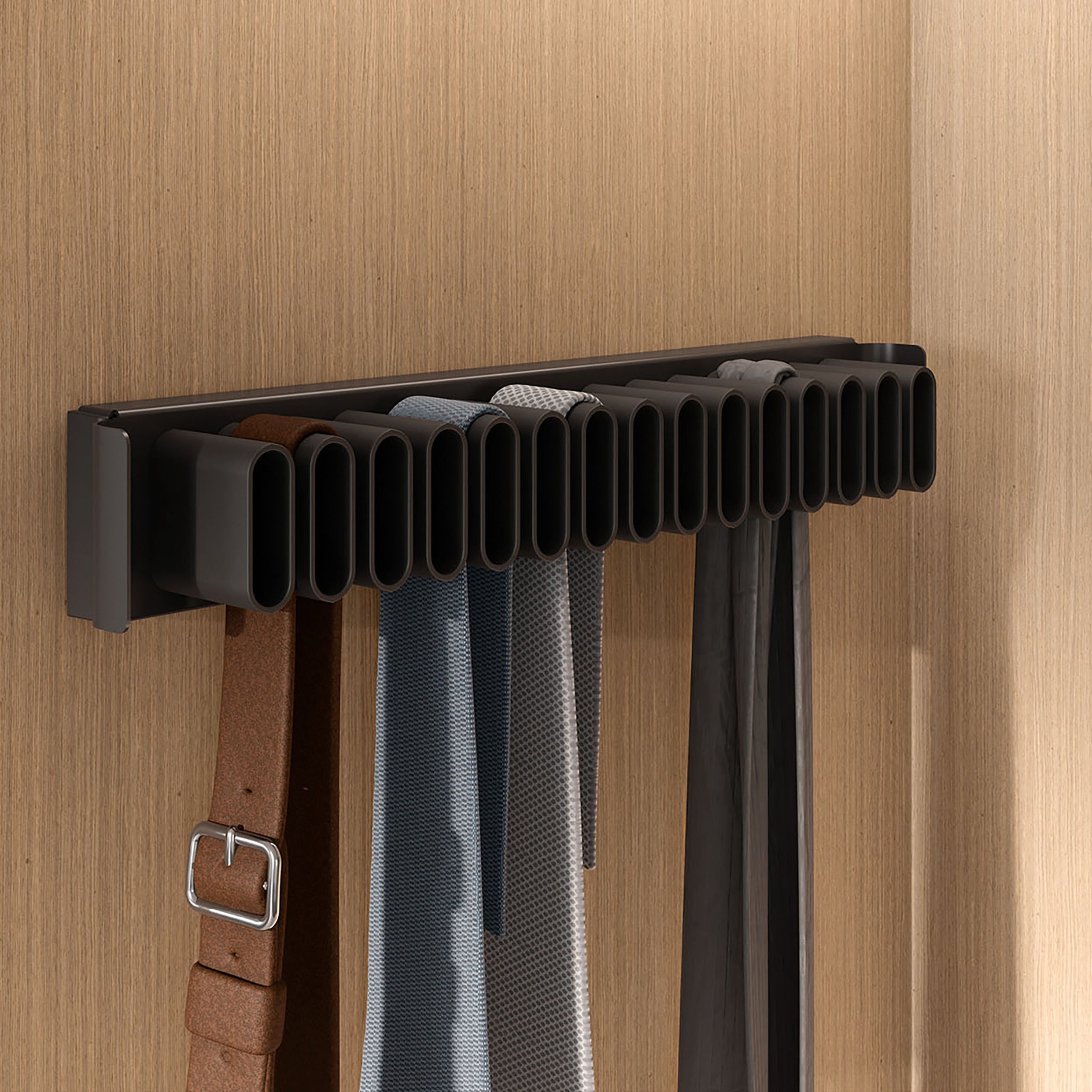 Ein schwarzer CONERO Gürtel- und Krawattenhalter (Auszug) mit mehreren Schlitzen hält mehrere Gürtel und Krawatten ordentlich vor einer hellen holzgetäfelten Wand.