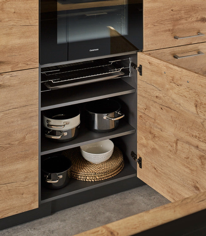 Geöffneter Unterschrank unter einem Backofen in einer Holzküche mit Backblechen und Töpfen