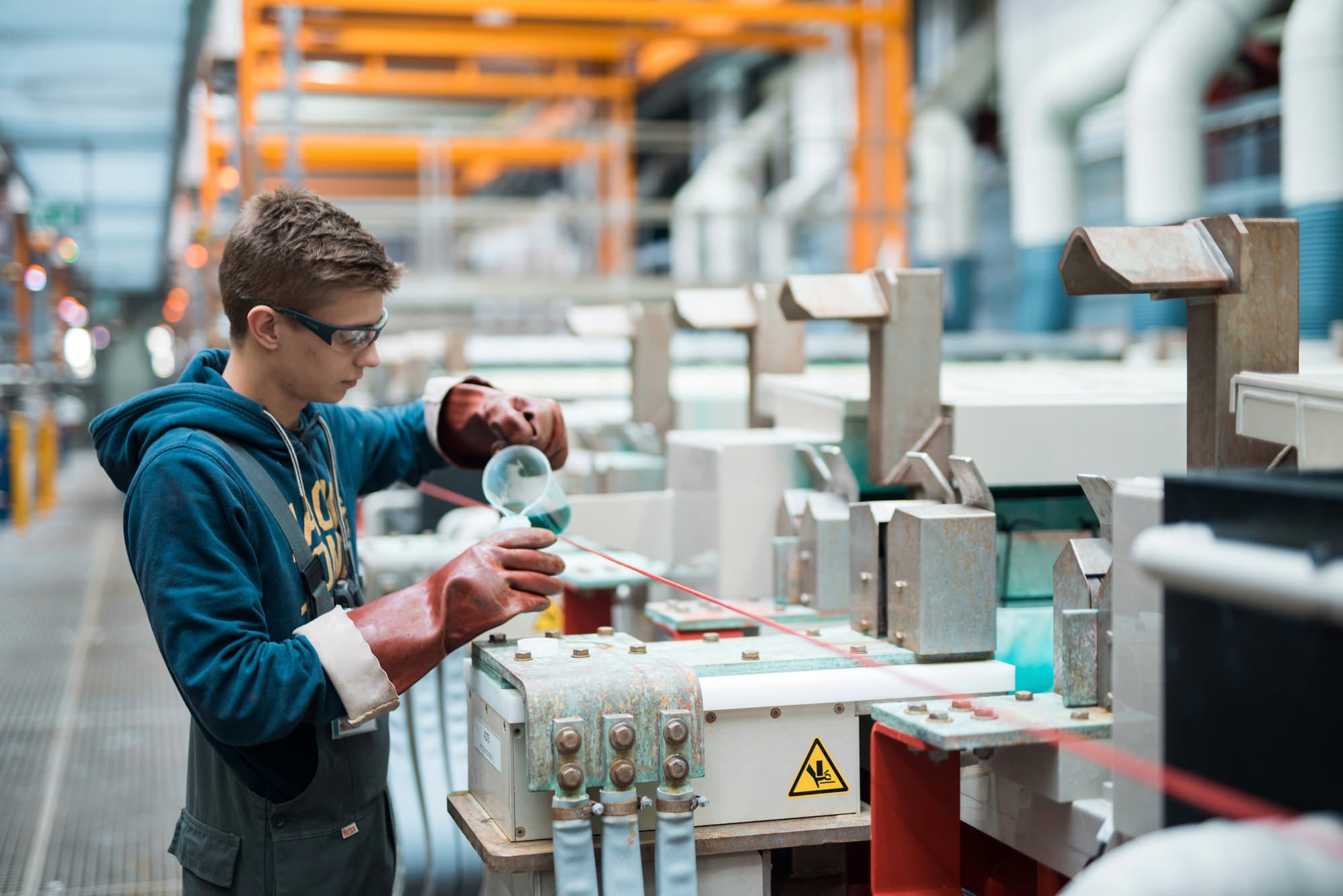 Arbeiter in Produktionshalle mit Arbeitshandschuhen füllt grüne Flüssigkeit in einen Behälter.