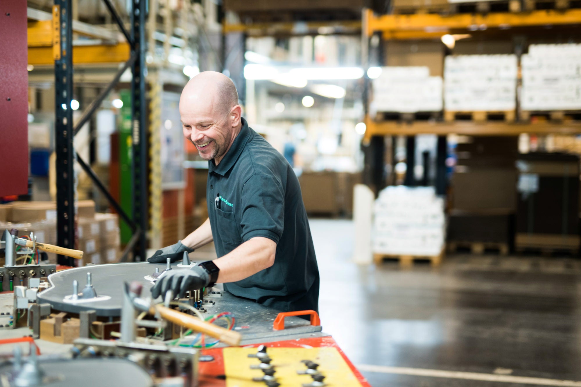 Arbeiter in Produktionshalle mit Poloshirt und Arbeitshandschuhen.