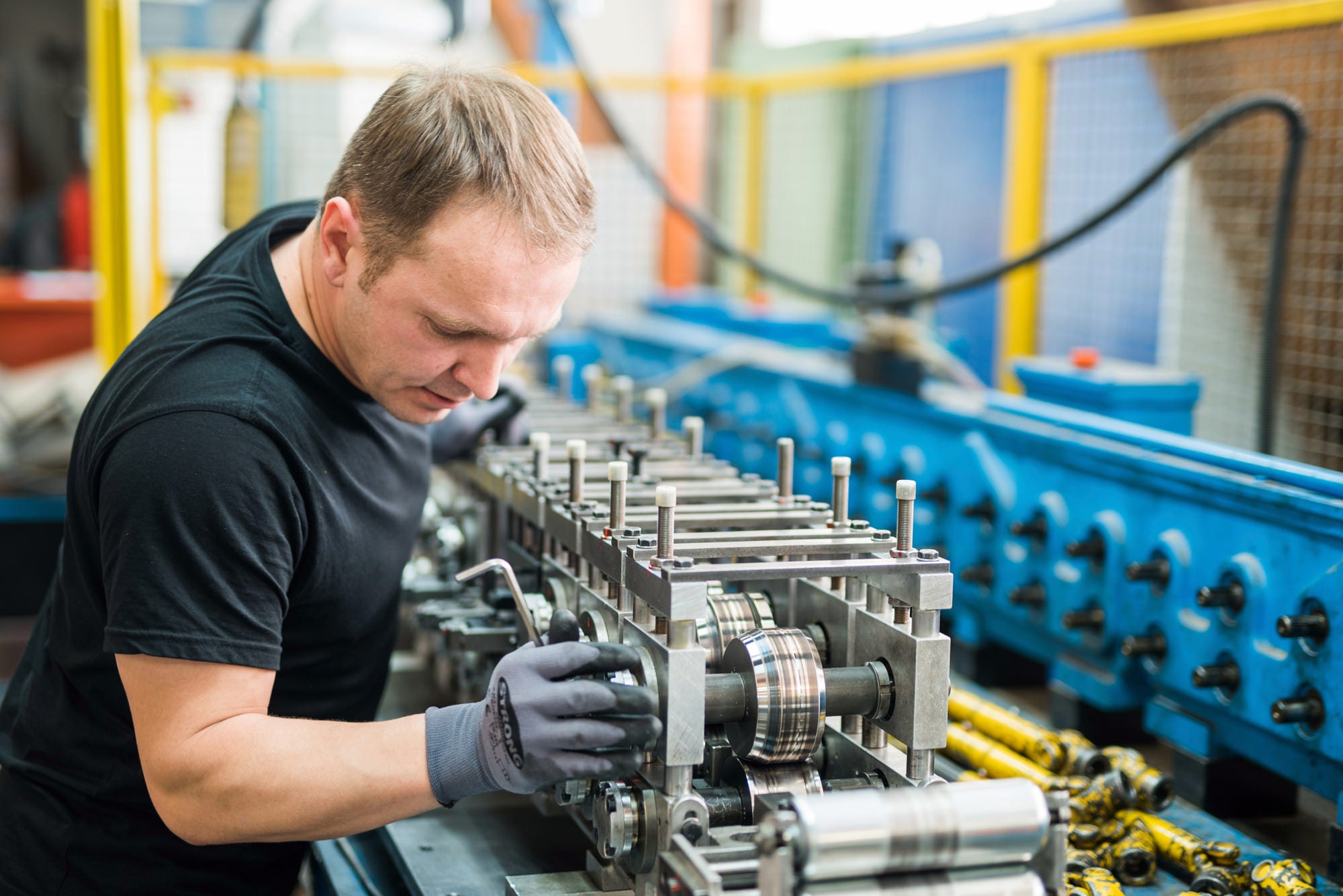 Arbeiter in Produktionshalle führt Arbeiten an einer Maschine aus.