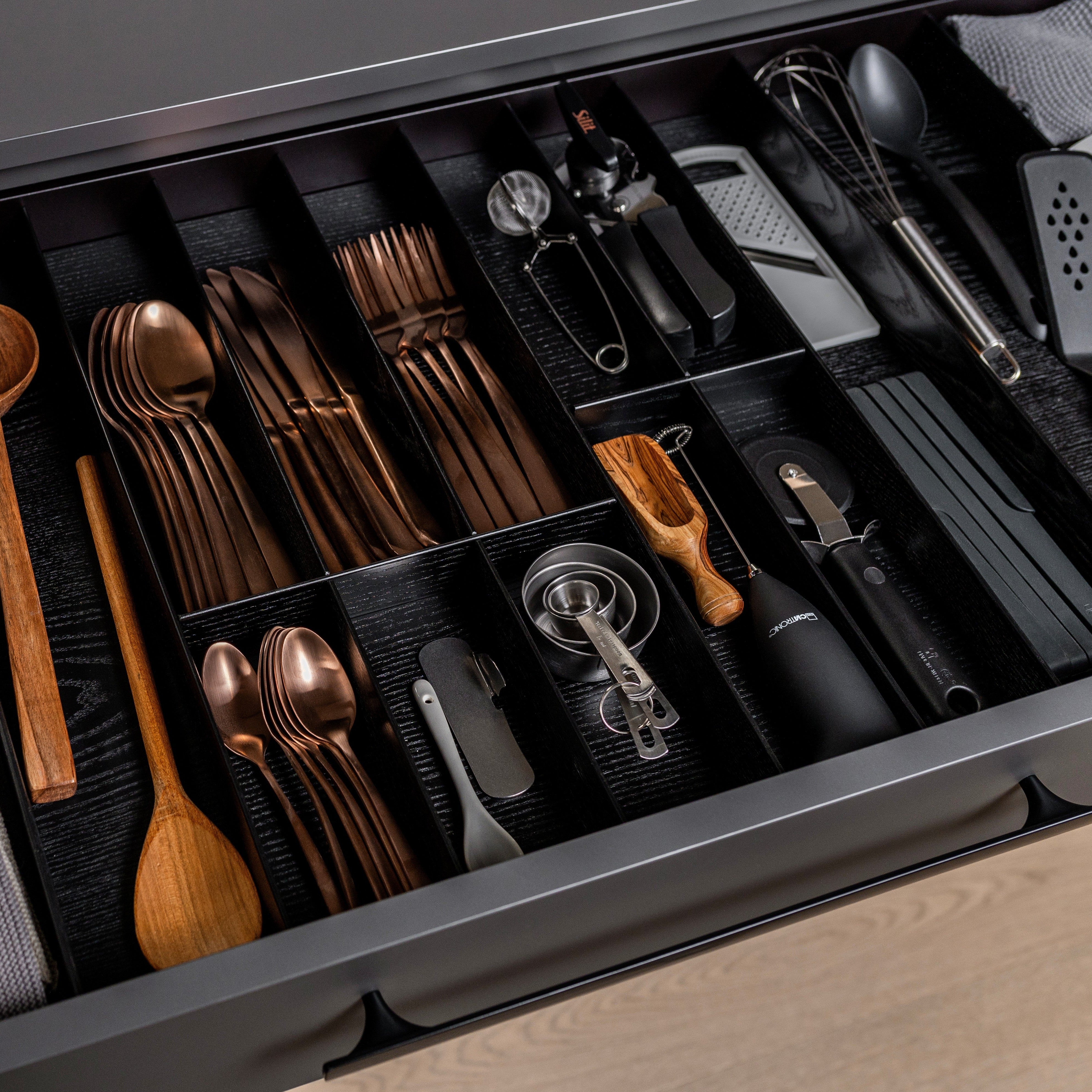 In der offenen Küchenschublade mit FineLine LiniQ Besteckeinsatz - Besteckkasten sind bronzefarbenes Besteck, Eschenholz-Utensilien, Messlöffel, Dosenöffner, Schneebesen, Sparschäler, Reibe und andere Werkzeuge für eine optimale Küchenorganisation übersichtlich angeordnet.
