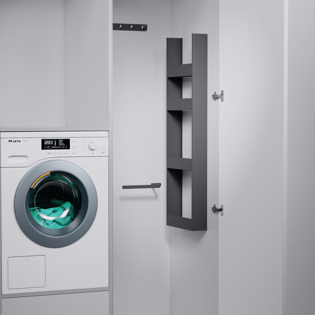 Eine weiße Frontlader-Waschmaschine befindet sich in einem eleganten, weißen Schrank. Daneben sorgt das seitliche EasyRack von K-Line mit Haken und Schienen an der Innenseite der Schranktür für eine intelligente Organisation des Hochschranks und eine effiziente Aufbewahrung.