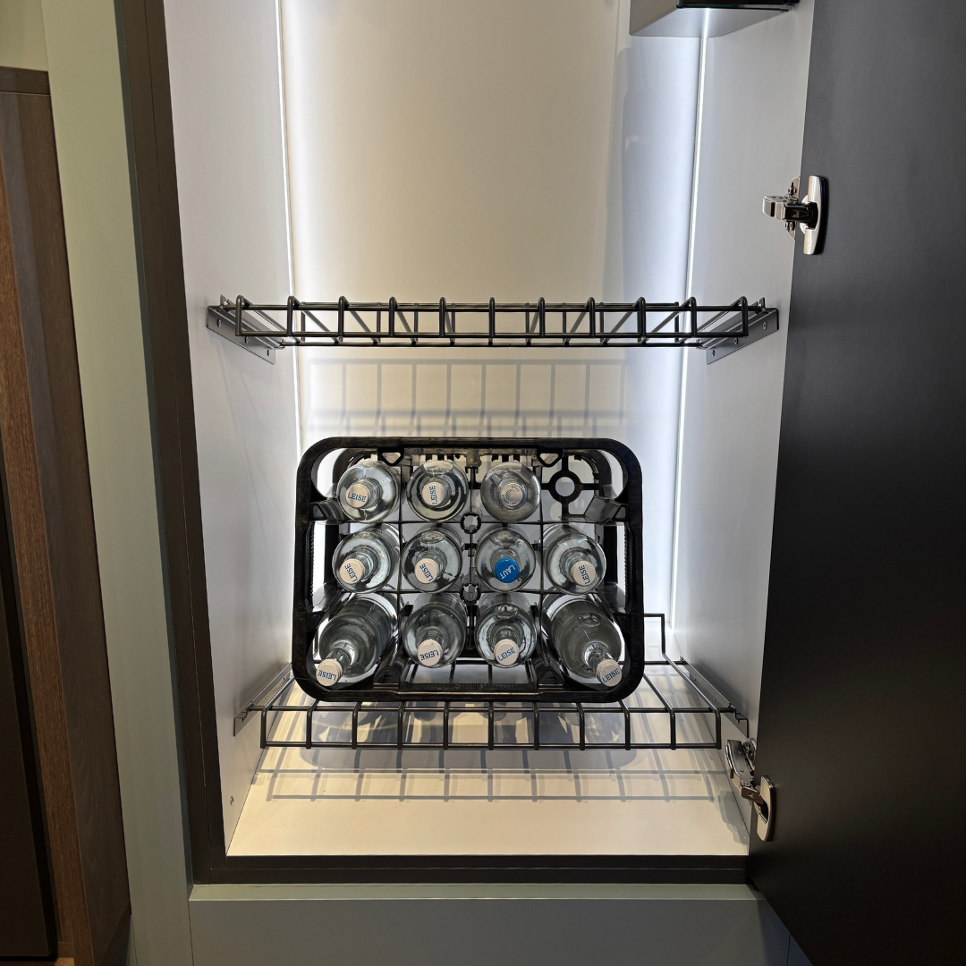 Ein offener Schrank mit einem Drahtboden zeigt das Ablage-Set für Getränkekisten - 600 mm, in dem eine schwarze Kiste mit klaren Glasflaschen mit silbernen Verschlüssen steht. Die Tür ist geöffnet und das beleuchtete Innere hebt die robusten Materialien des Sets hervor.