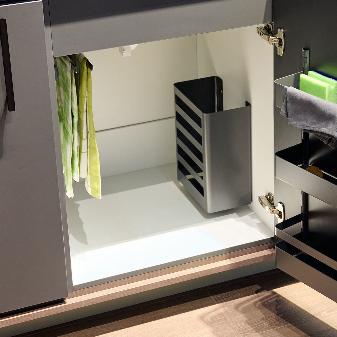 Offener Küchenschrank mit vertikalem schwarzem Ordnungssystem, grün gestreiften Geschirrtüchern auf der linken Seite, einer seitlichen K-Line Utensilienbox für Spülschwämme und einem modernen, klaren Design.