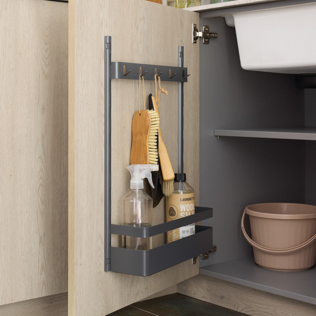 Die seitliche Befestigungsleiste von K-Line bietet Platz für Reinigungsbürsten, eine Sprühflasche und Reinigungsmittel in einem hellen Holzschrank mit einem rosafarbenen Eimer darunter und einem weißen Waschbecken darüber - ideal für eine geordnete Aufbewahrung.
