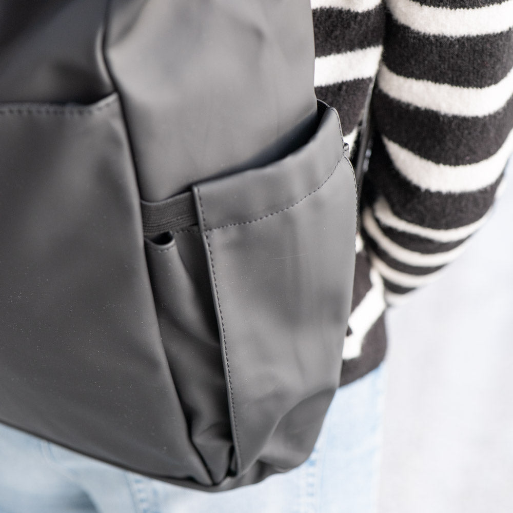 Eine Person, die einen schwarz-weiß gestreiften Pullover und hellblaue Jeans trägt, hat den Kesseböhmer Rucksack mit einer praktischen Seitentasche dabei - perfekt für Mahlzeiten to go. Das Bild hebt dieses praktische Rucksack-Detail hervor.