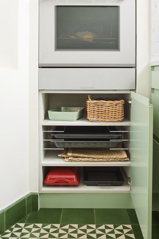 Weißer Backofen über einem offenen Unterschrank mit mehreren Fächern. Der Unterschrank enthält Auflaufformen und Backbleche.