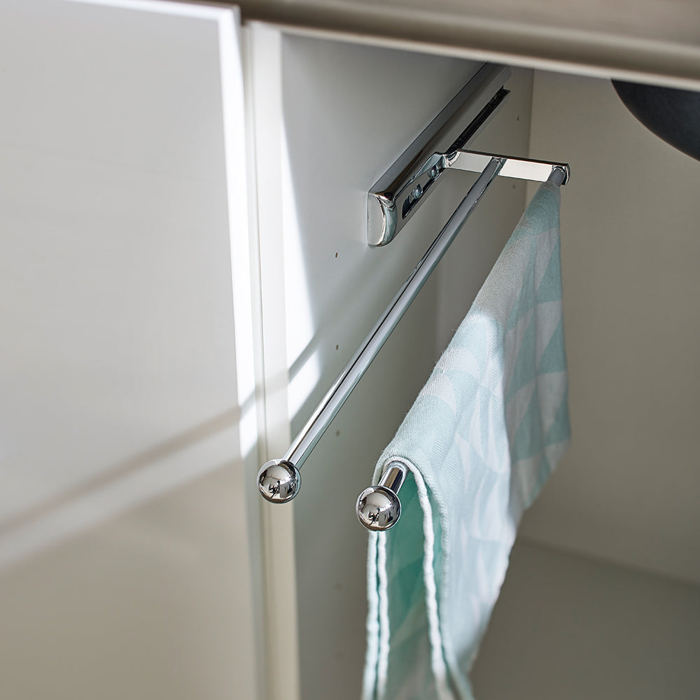 Der Handtuchauszug - ein ausziehbarer Handtuchhalter - ist in einem weißen Küchenschrank montiert und hält ein hellblau gemustertes Handtuch. Die offene Tür zeigt den platzsparenden Halter für Küche und Bad.