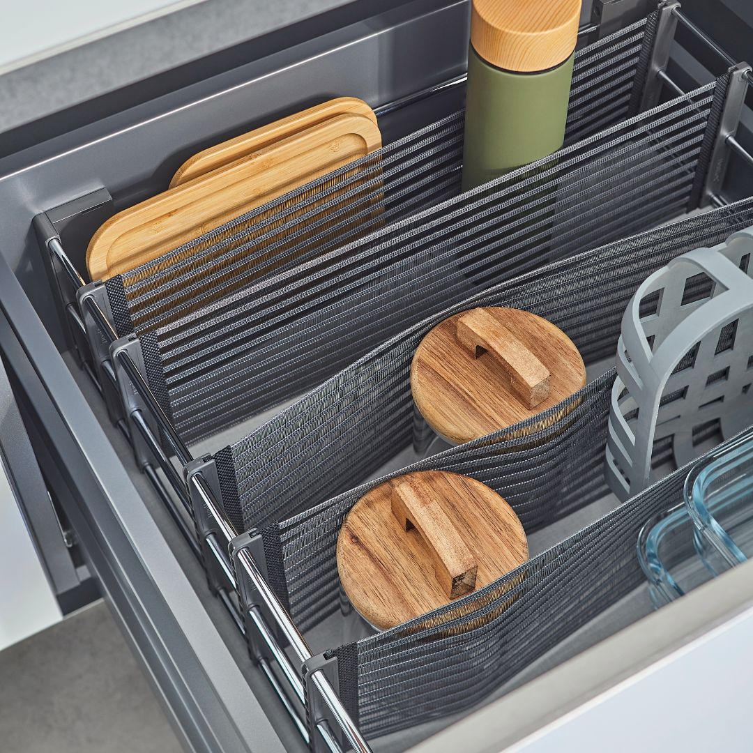 In einer Küchenschublade, die mit dem SpaceFlexx® Schubladen Organizer organisiert wurde, finden zwei hölzerne Schneidebretter, eine grüne Flasche, zwei Gläser mit Holzdeckeln, ein grauer Utensilienhalter und ein Glasbehälter Platz - alles in Deutschland hergestellt.
