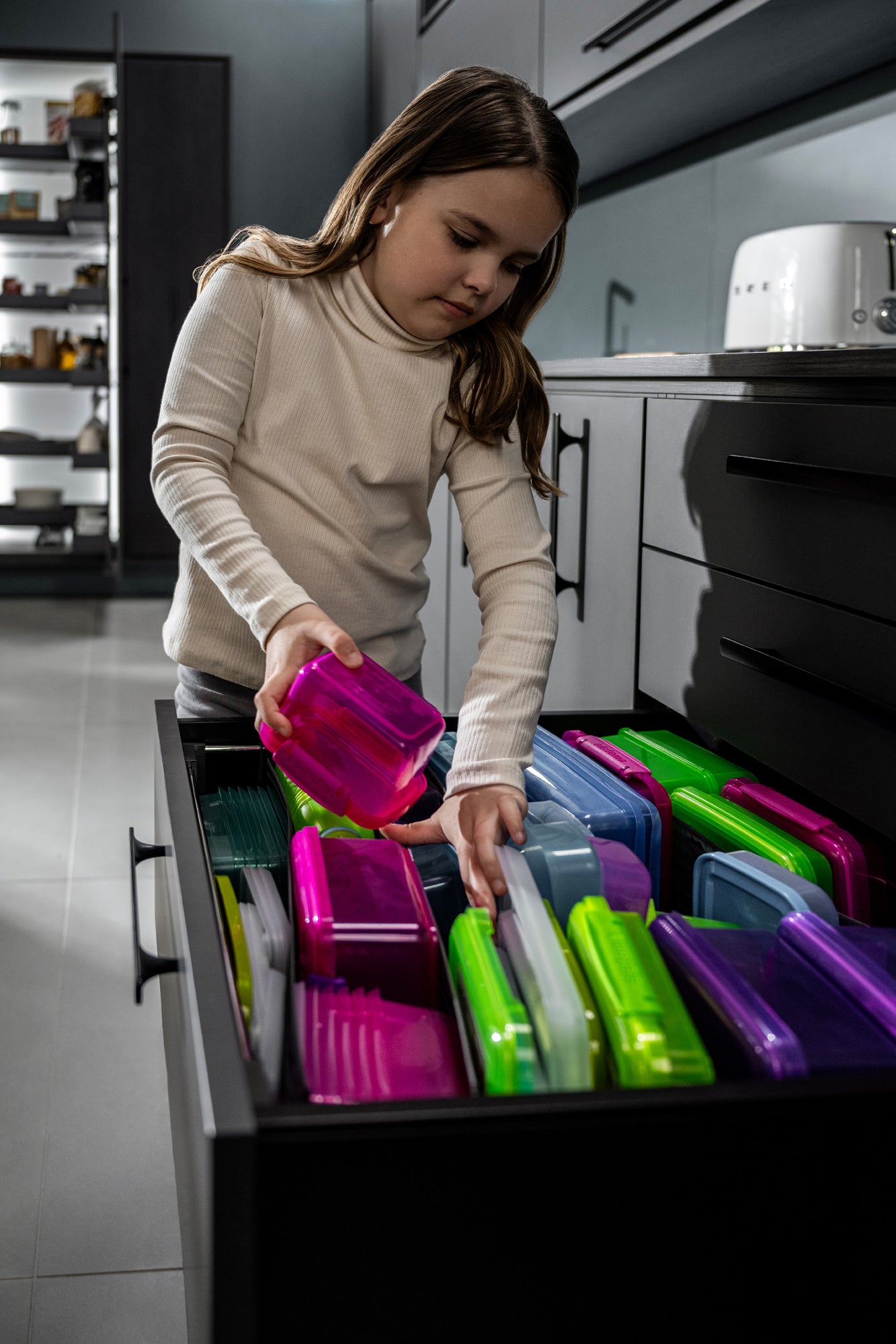Kind sortiert bunte Dosen in eine geöffnete Schublade mit Schubladenorganizer ein.