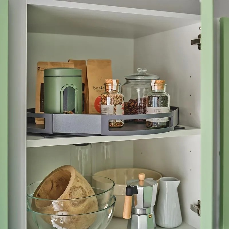 Geöffneter Hängeschrank in grüner Küche mit einem auf Zwischenboden montierten Drehtablar mit verschiednen Gewürzen.