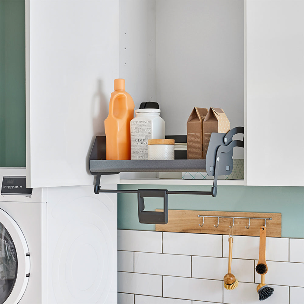 Das iMove 60er single Auszugsystem für den Hängeschrank schafft im weißen Küchenschrank Ergonomie: Flaschen und Kartons sind über der Waschmaschine verstaut, Reinigungsutensilien hängen griffbereit an einer Leiste.