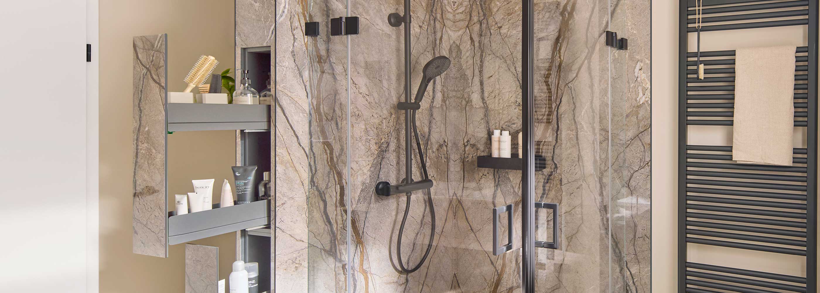 Ein modernes Badezimmer mit einer Glasduschkabine, Marmorwänden, einer schwarzen Duscharmatur und Ablagen für Toilettenartikel. An der rechten Wand ist ein schwarzer Handtuchheizkörper mit einem beigen Handtuch angebracht.