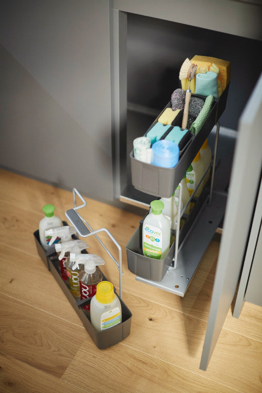 Geöffneter Unterschrank mit herausgezogenem Putzmittelauszug von oben. Auf dem Fußboden daneben ein herausnehmbarer Korb.