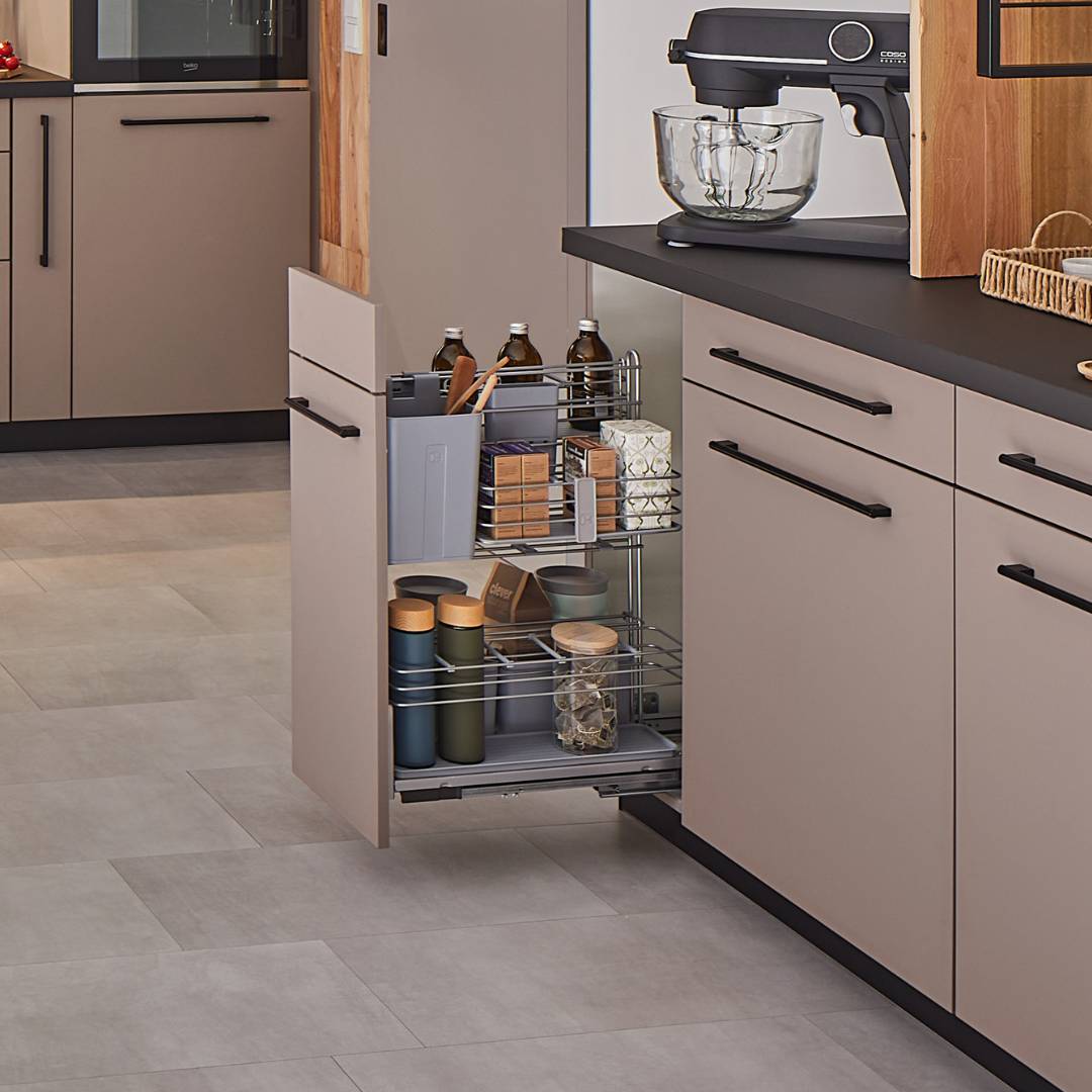 Eine moderne Küche mit beigen Schränken mit schwarzen Griffen, einer schwarzen Arbeitsplatte und einem cookingAGENT - kleiner Apothekerschrank & Küchenauszug, der Gläser und Flaschen aufnimmt. Auf dem Tresen darüber steht ein Standmixer.