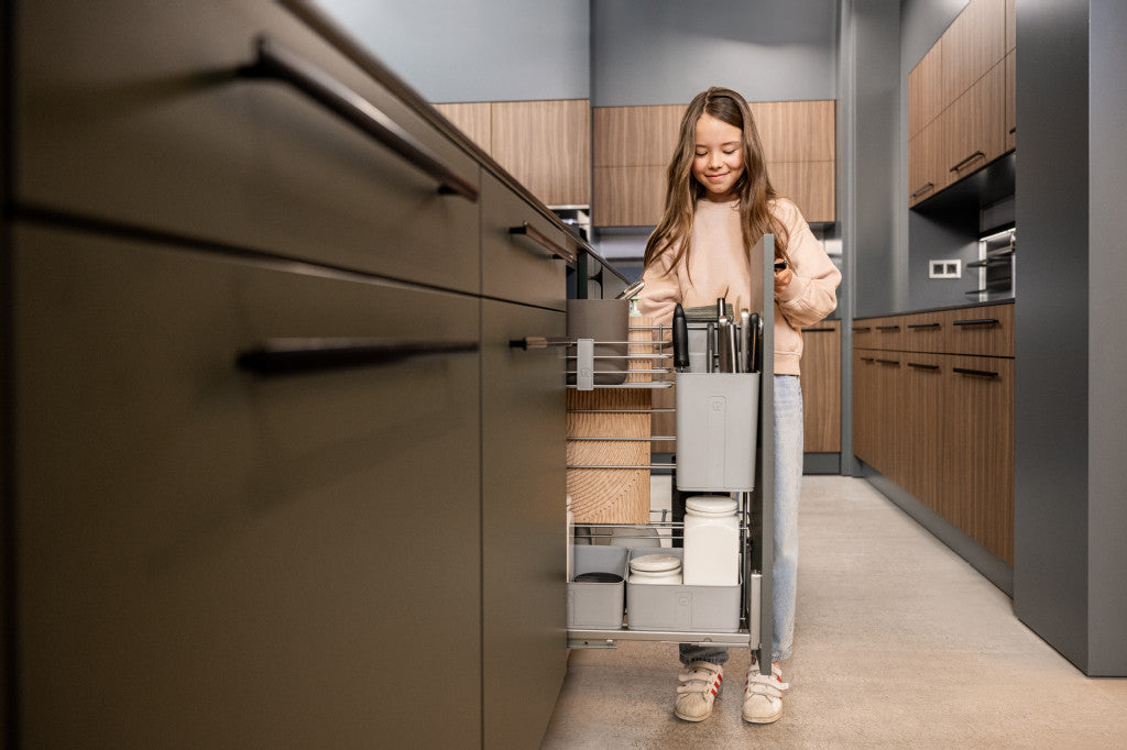 Kind räumt einen ausziehbaren Kpchenunterschrank mit Vorräten ein. Der Schrank hat verschieden Boxen und Einteilungen.