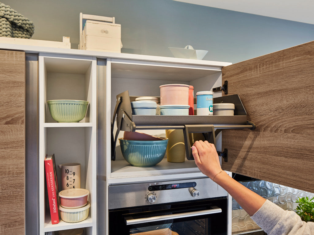 Dunkelgraues Auszugsystem im Hängeschrank wird von einer Hand am Griff nach unten geschwenkt.