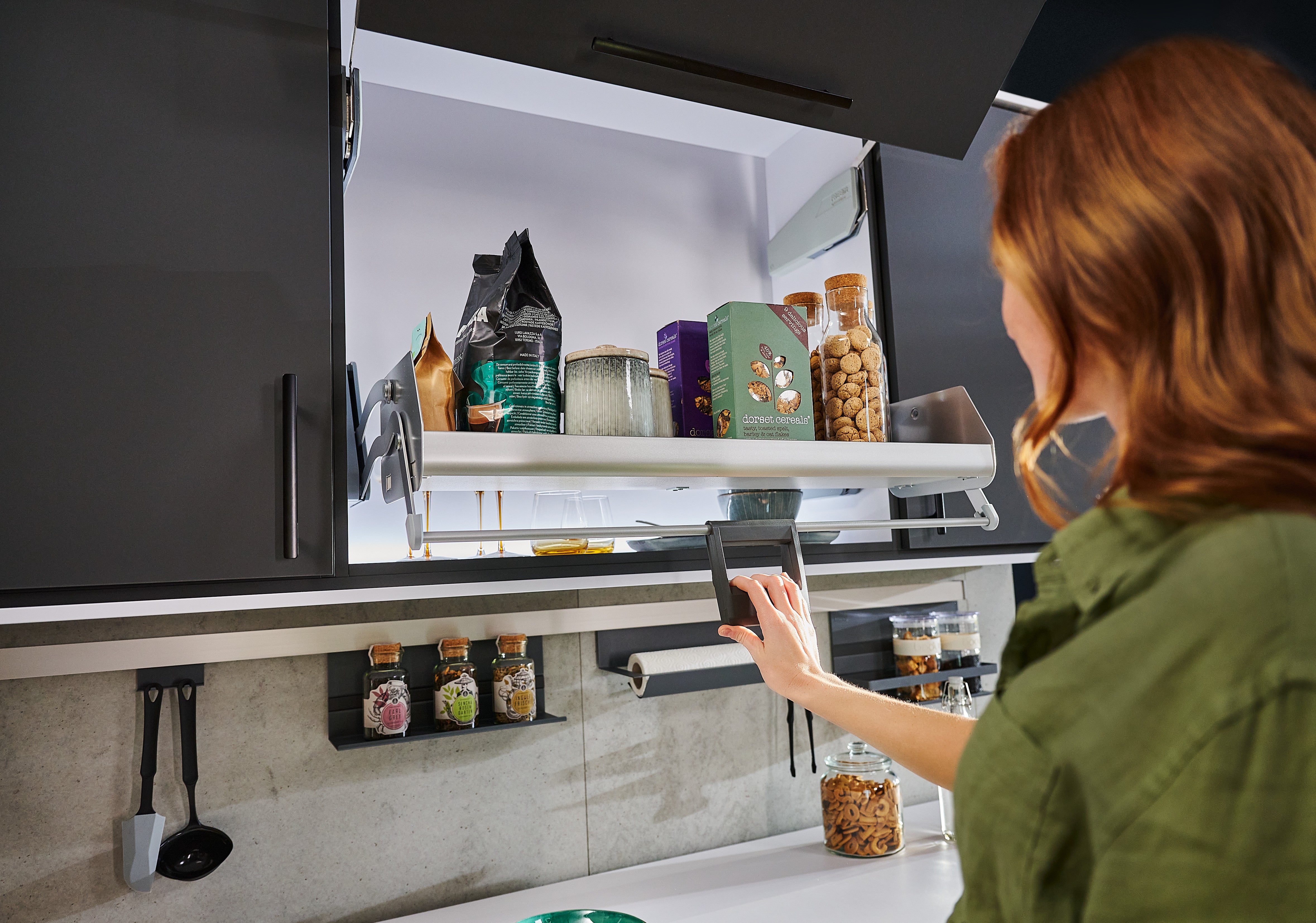 Junge Frau in dunkler Küche bedient einen herunterschwenkbaren Auszug im Hängeschrank.