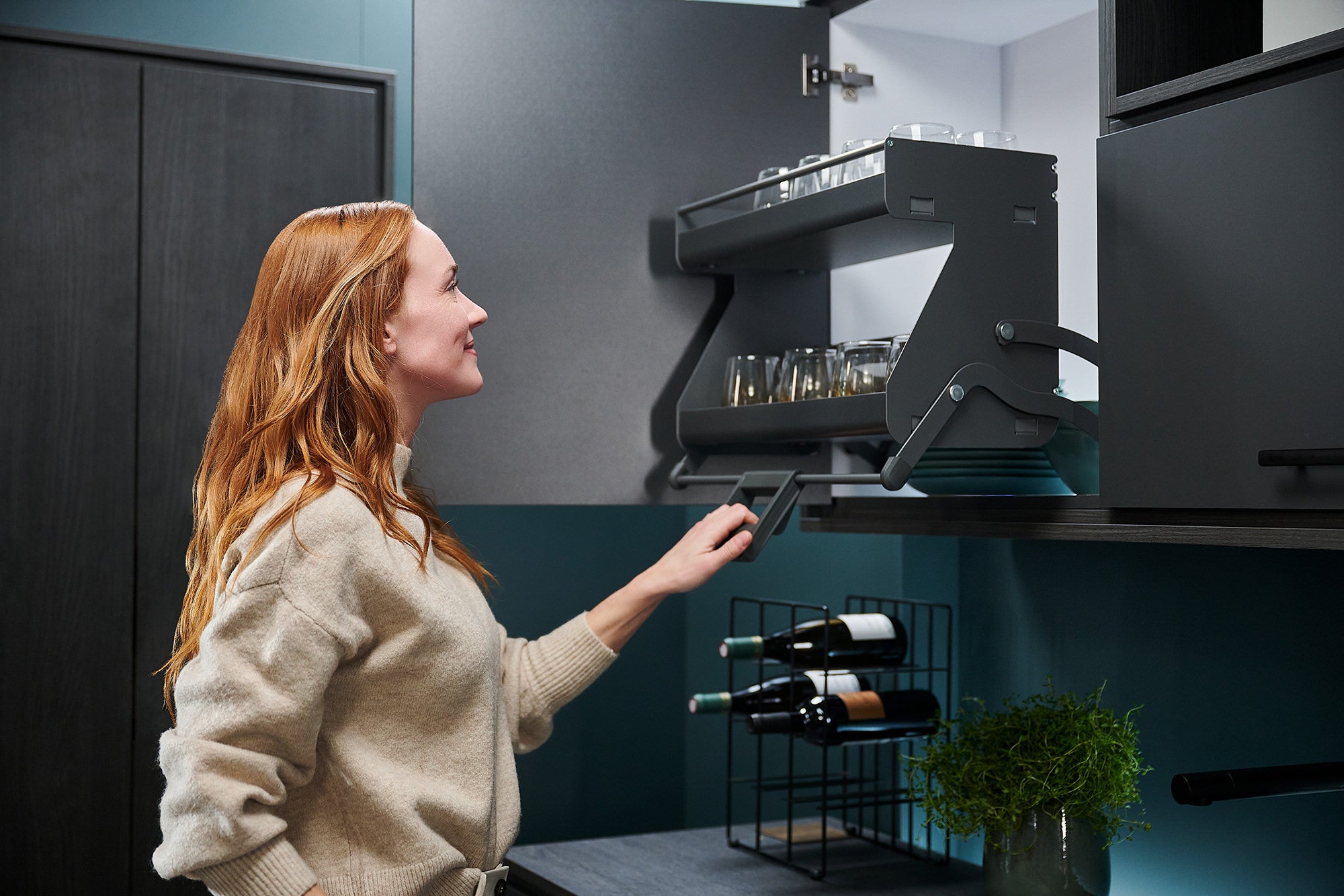 Dunkelgraues Auszugsystem im Hängeschrank wird von einer Frau am Griff nach unten geschwenkt.