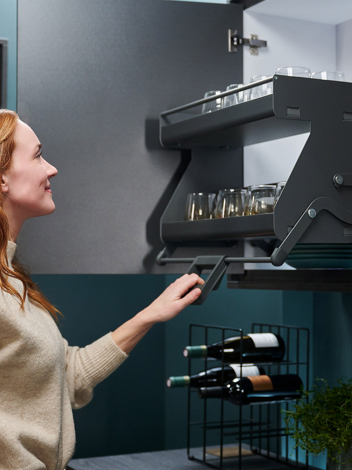 Dunkelgraues Auszugsystem im Hängeschrank wird von einer Frau am Griff nach unten geschwenkt.