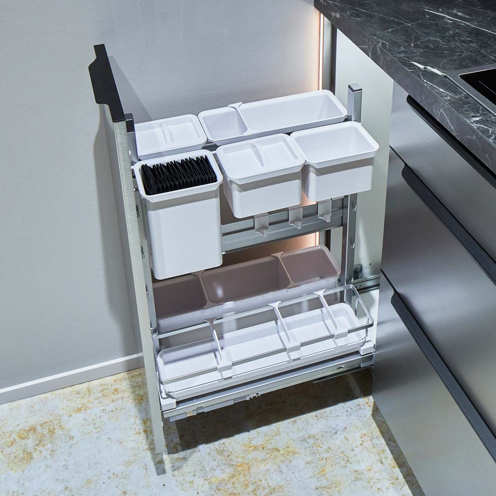 Eine moderne, ausziehbare Küchenschublade mit mehreren weißen Kunststofffächern für Utensilien und Kleinteile, installiert in einem schlichten grauen Schrank neben einer Marmorarbeitsplatte.