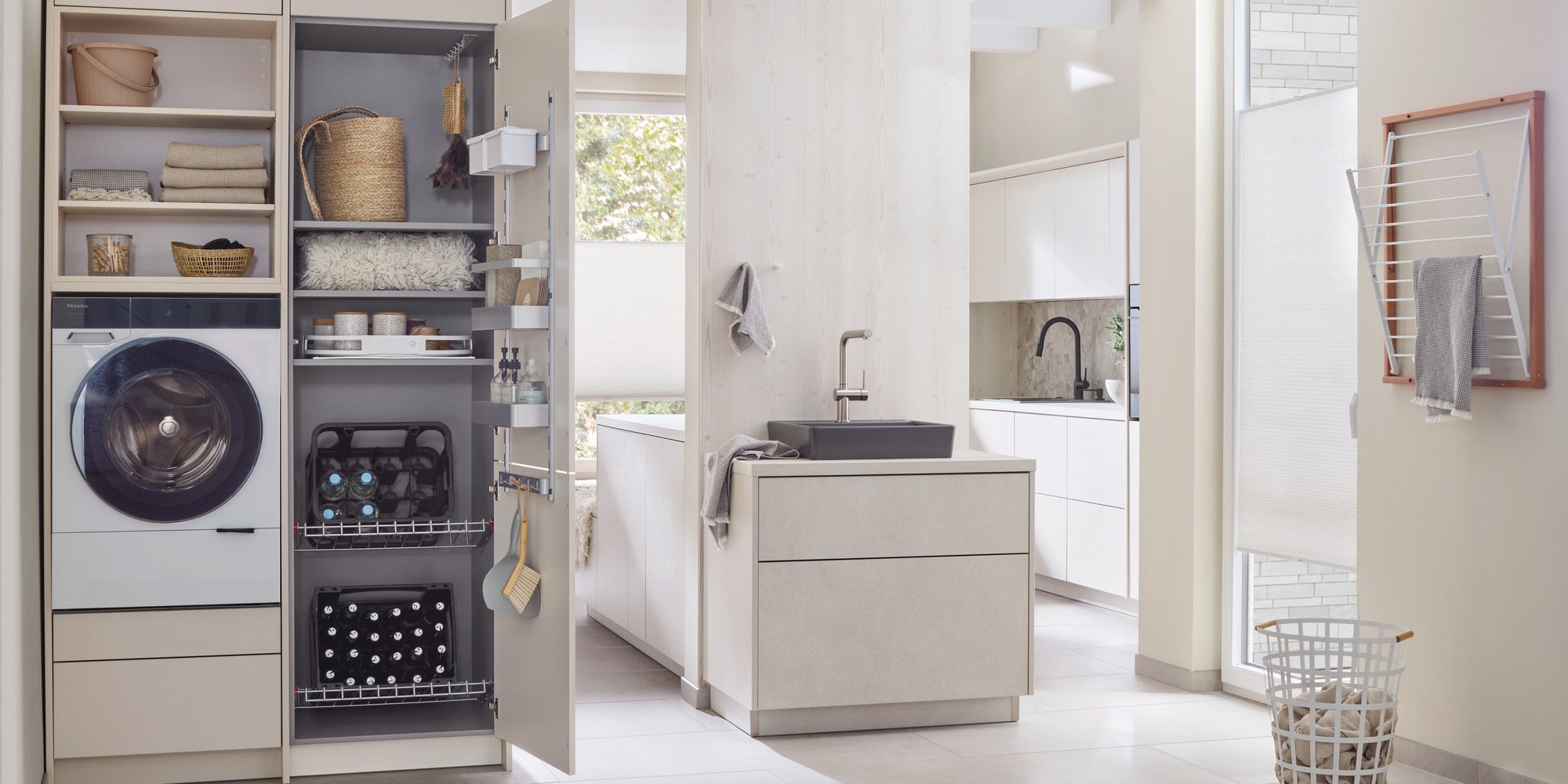 Moderne Waschküche mit offenem Schrank mit Waschmaschine, Regalen mit Körben, Handtüchern und Reinigungsmitteln, daneben ein helles Bad mit Waschbecken und Handtuchhalter.