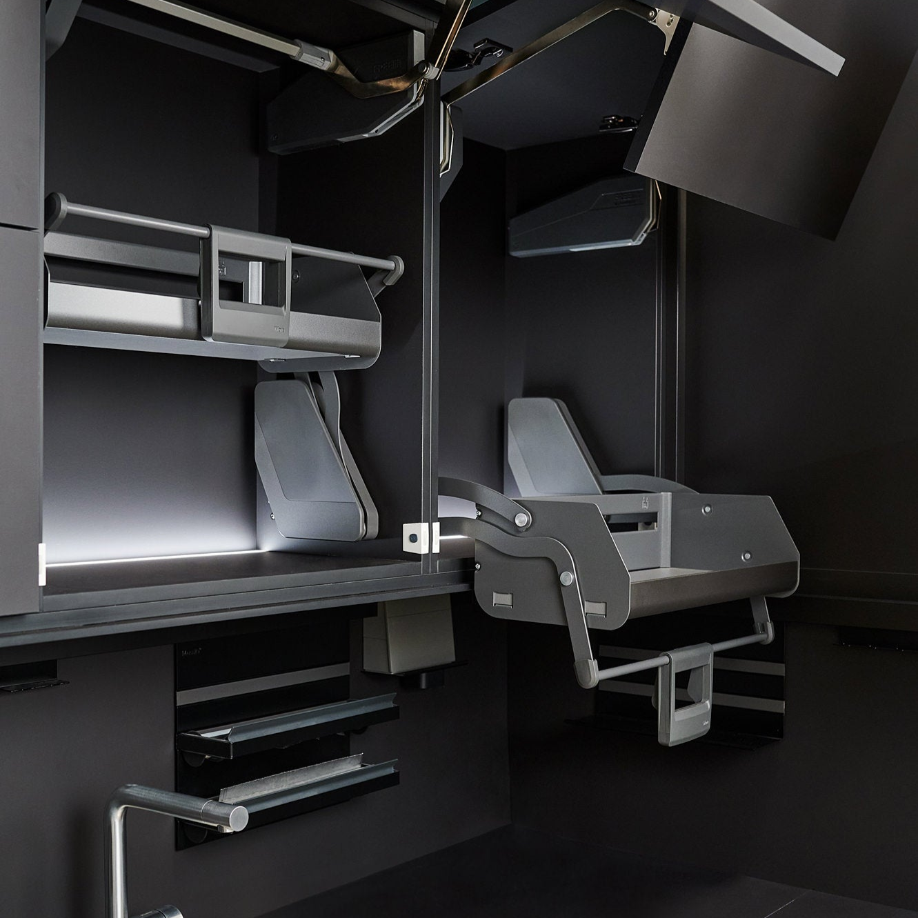 Ein modernes, minimalistisches Zimmer ist mit eleganten, faltbaren Möbeln ausgestattet, darunter ein Hochbett, ein umwandelbarer Schreibtisch und ein an der Wand befestigter Stuhl, alles in dunklen Grautönen mit metallischen Akzenten.