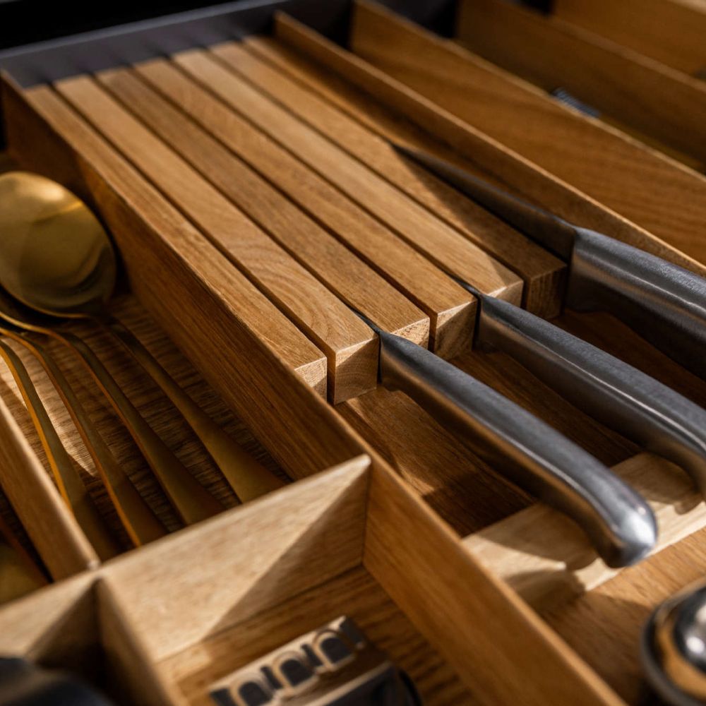 Eine Nahaufnahme des FineLine LiniQ Messerblocks, einem hölzernen Küchenschubladen-Organizer für Küchenorganisation, der Messer mit Metallgriffen und goldfarbene Utensilien übersichtlich in separaten Fächern für Messer sicher verstauen zeigt.