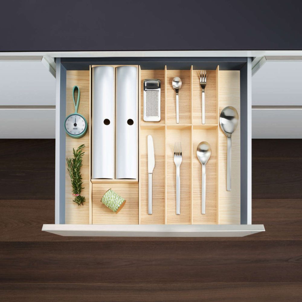 Öffnen Sie eine Küchenschublade, die mit dem FineLine LiniQ Folienhalter organisiert ist. Er hält Utensilien in hölzernen Teilern - Schneebesen, Reibe, Sparschäler, Schere, Pergamentrollen, Frischhaltefolien, frische Kräuter und robuste Schnur - ideal für moderne Küchen.