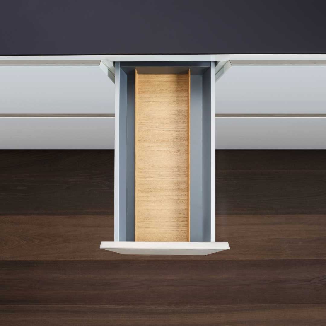 Draufsicht auf eine offene, leere Schublade mit Holzinnenleben, ideal für die Küchenorganisation mit dem FineLine LiniQ Multifunktionseinsatz - Schubladen Organizer, eingebettet in einen weißen Schreibtisch auf einem dunkelbraunen Holzboden.