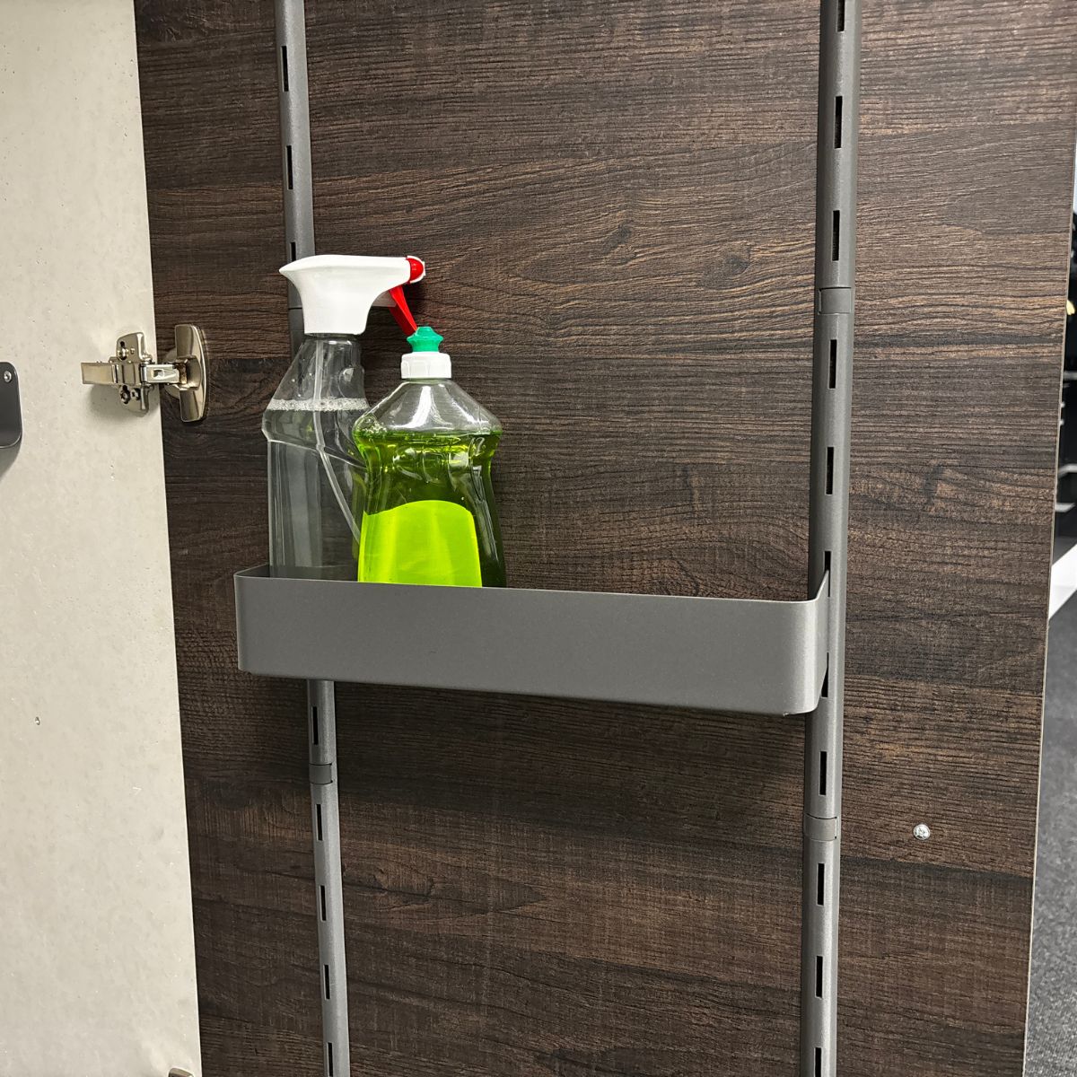 An einer dunklen Holzwand ist eine höhenvariable K-Line-Seitenablage montiert, die eine klare Sprühflasche und eine grüne Spülmittelflasche mit grünem Verschluss hält.