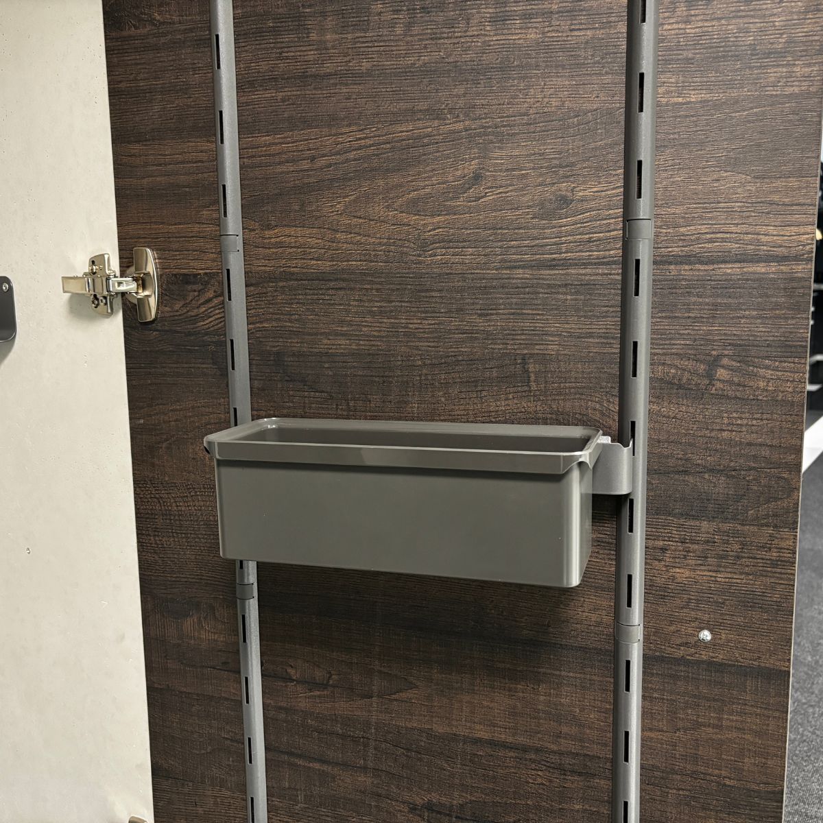 Die K-Line side Trägerleiste mit Box in Grau ist an einem vertikalen Metallrahmen auf einer dunklen Holzplatte mit Silber-Scharnier links montiert - ideal, um den Küchenschrank zu organisieren.