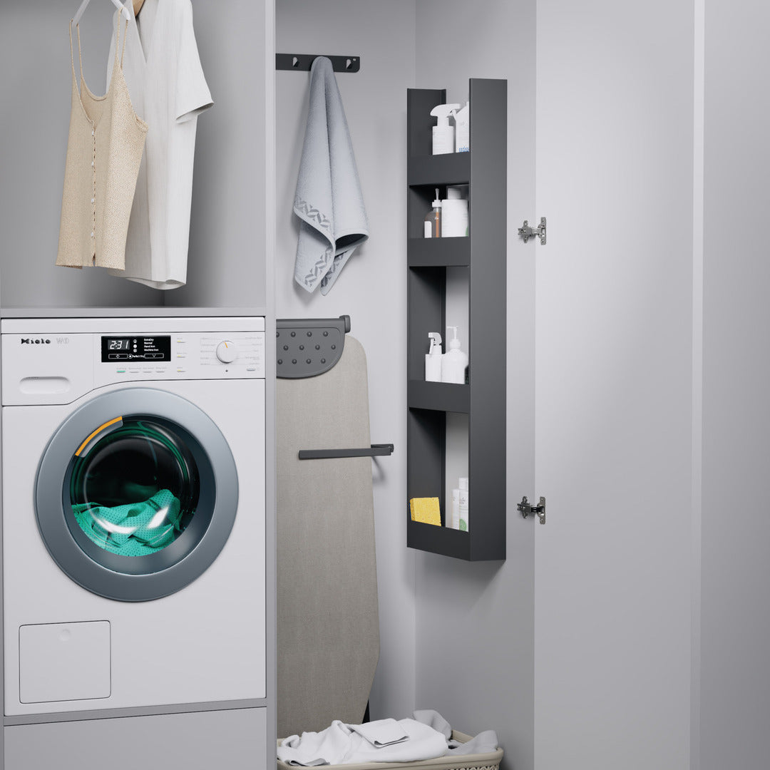 Eine moderne Waschküche verfügt über eine Frontlader-Waschmaschine, gefaltete Handtücher, ein Bügelbrett und hängende Wäsche. Das seitliche K-Line EasyRack an der Wand bietet zusätzlichen Hochschrank Organisation für Waschmittel und Reinigungsmittel.