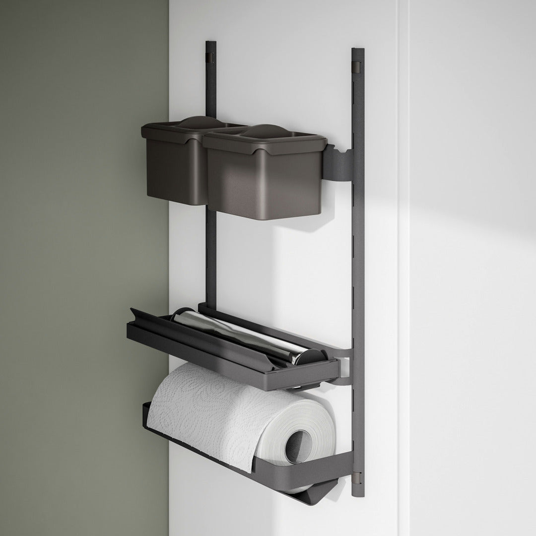 Die K-Line Seite ROLLINERO - Rollenablage ist eine Wandablage mit zwei grauen Behältern auf der oberen Ablage, einer mittleren Ablage für Folie oder Frischhaltefolie mit Schneidekante und einer unteren Ablage für Papierhandtücher, alles auf einer weißen und grünen Wand.