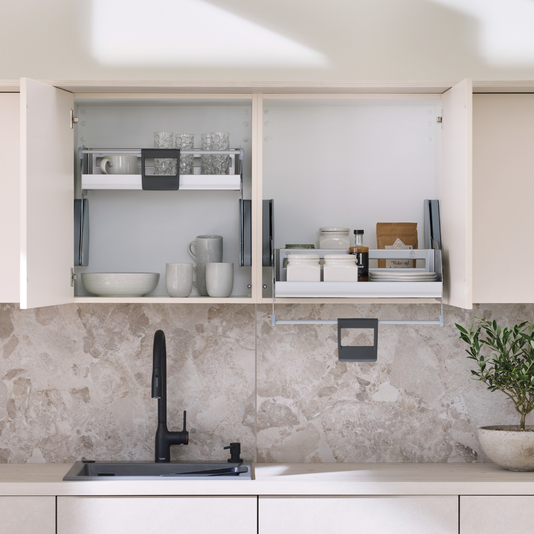 In einer modernen Küche mit iMove 60er single - Auszugsystem für den Hängeschrank sind Geschirr und Gläser übersichtlich angeordnet. Darunter ein schwarzer Wasserhahn über dem Spülbecken, eine Marmorplatte und eine kleine Topfpflanze - ideal für die ergonomische Aufbewahrung.